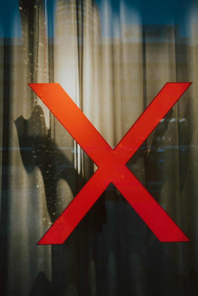 pexels photo 11296590 11296590 A striking red X on a glass window with intriguing shadows behind, creating a mysterious scene.