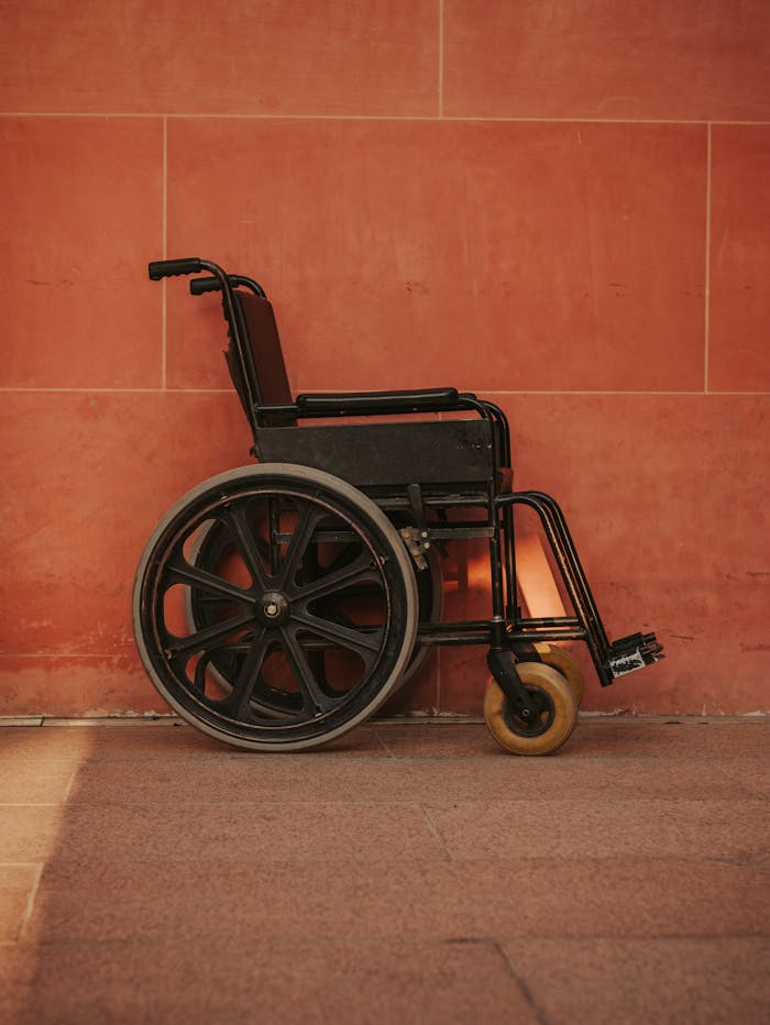 About A black wheelchair stands against a striking red wall, highlighting urban accessibility themes.