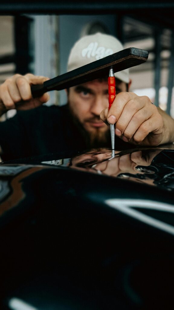 Mechanic expertly repairing car dent using specialized tool in workshop.